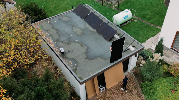 Luftaufnahme eines Wohnhauses mit Solarmodulen auf dem Flachdach und Monteur bei der Installation